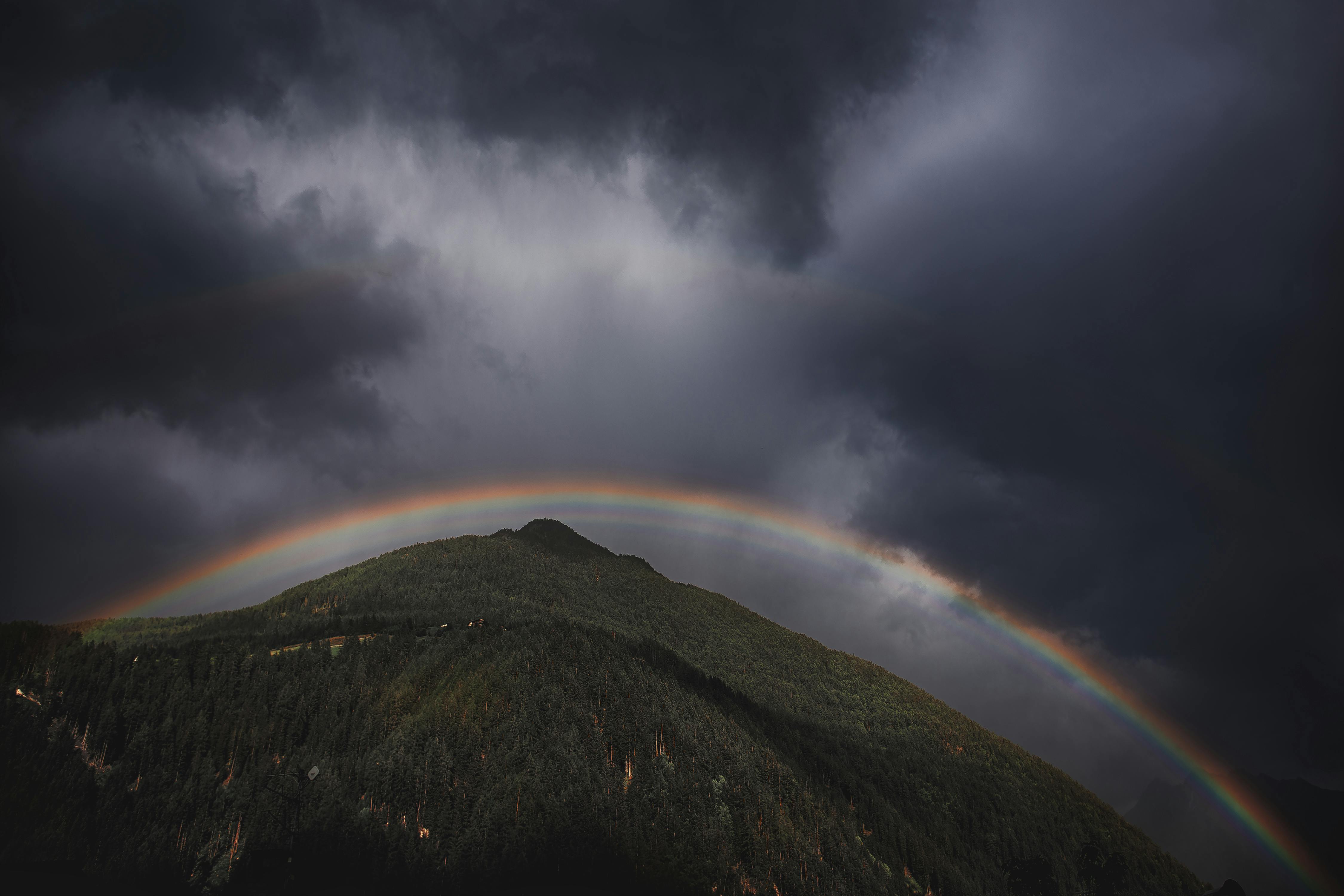 A rainbow in the sky above a mountain on a very cloudy day